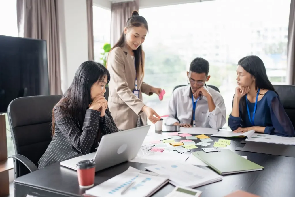 Groupe en réunion autour de table avec documents, image illustrant la réflexion sur le choix entre EI et EURL pour créer une entreprise.
