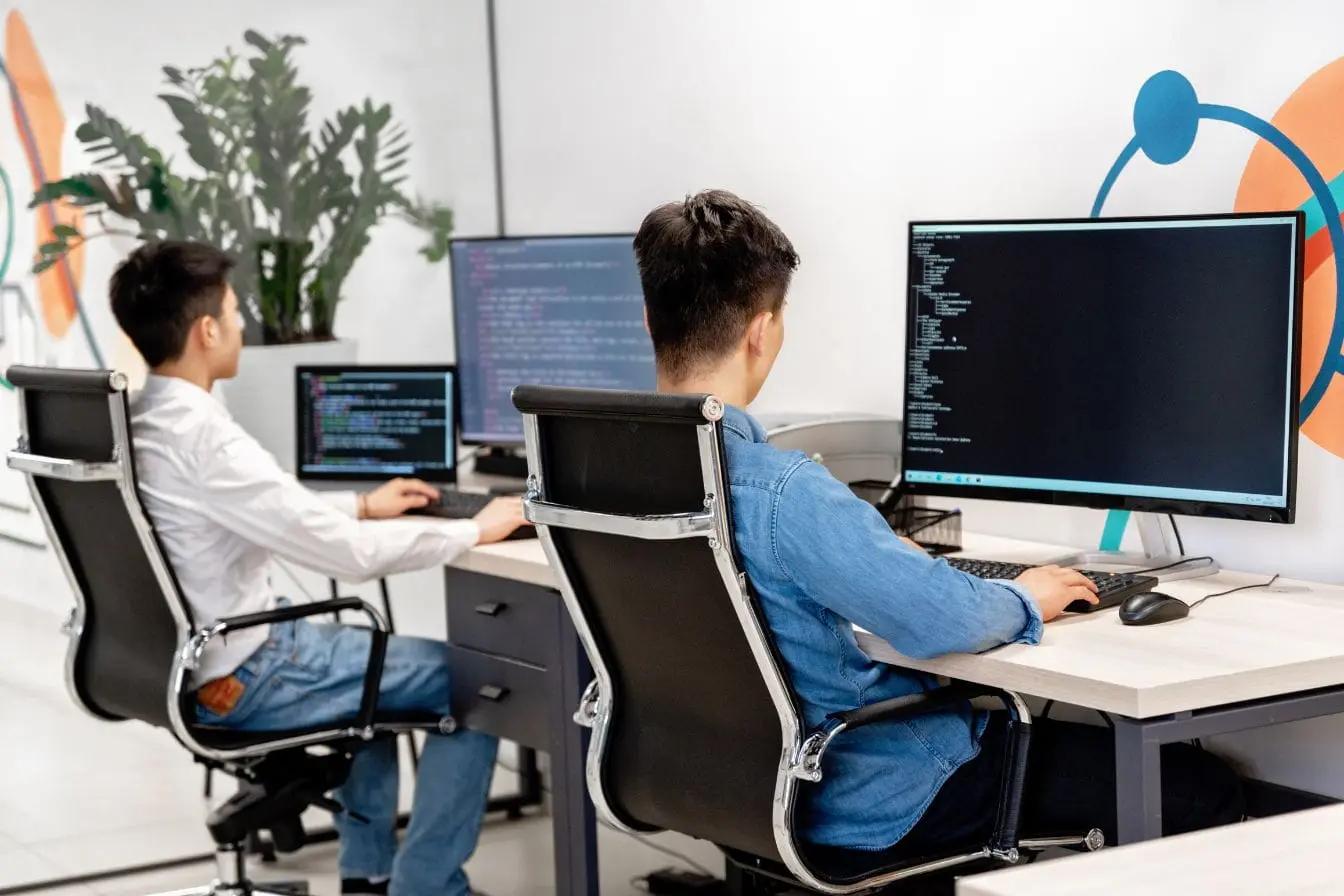 Deux personnes concentrées devant grands écrans affichant du code, image qui illustre la protection d’un site web contre les cyberattaques.