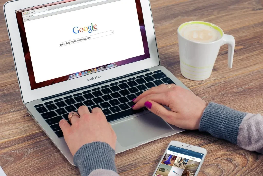 Personne tapant sur MacBook Air affichant recherche Google, reflet des critères E-E-A-T pour fiabilité et expertise du contenu.