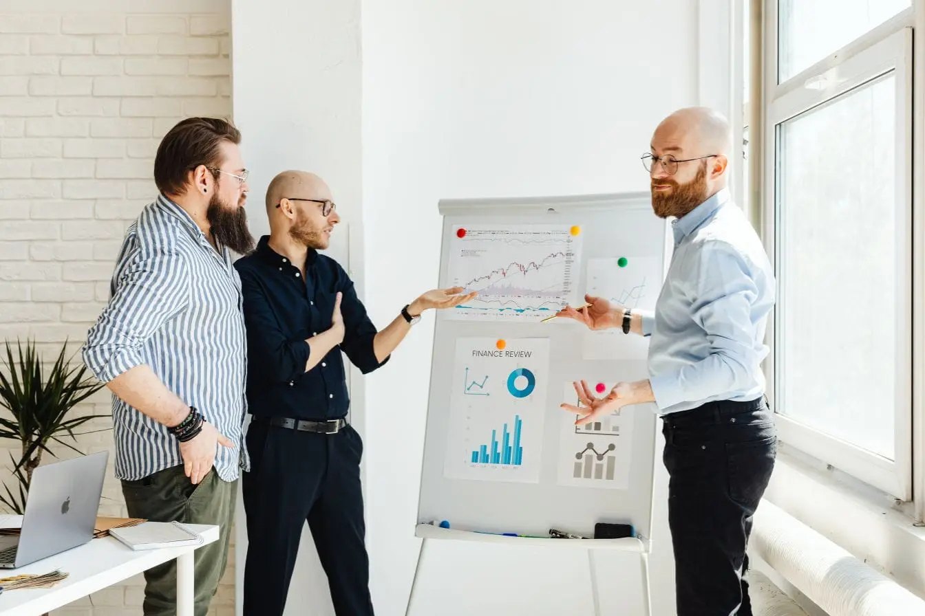 Trois collègues en réunion devant tableau rempli de graphiques, image qui illustre la stratégie Product-Led Growth et son impact sur la croissance.