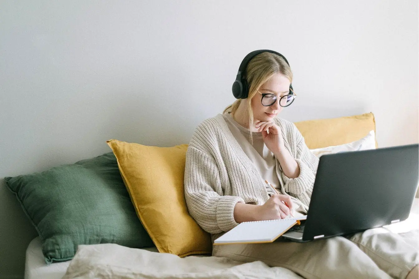 UX writing Personne concentrée avec casque et lunettes écrivant sur carnet devant laptop, image qui illustre la pratique du UX writing.