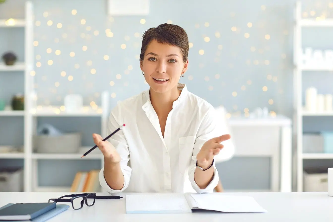 Personne en chemise blanche expliquant avec gestes devant bureau, image qui illustre la posture d’un mentor guidant par expérience face à un coach orienté action.