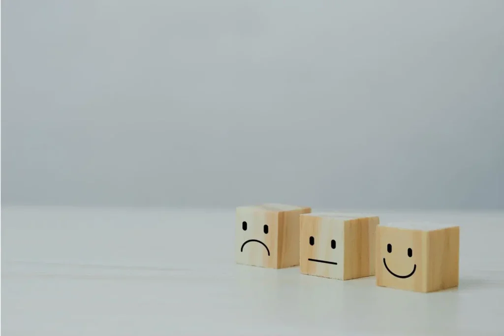 Trois cubes en bois alignés affichant des visages triste, neutre et heureux, image qui illustre la gestion de sa e‑réputation selon les retours reçus.