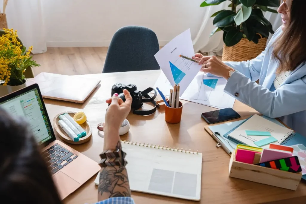 Deux personnes discutent autour d’un tableau de ventes et d’un ordinateur, image qui illustre la collaboration nécessaire pour créer une marque blanche.