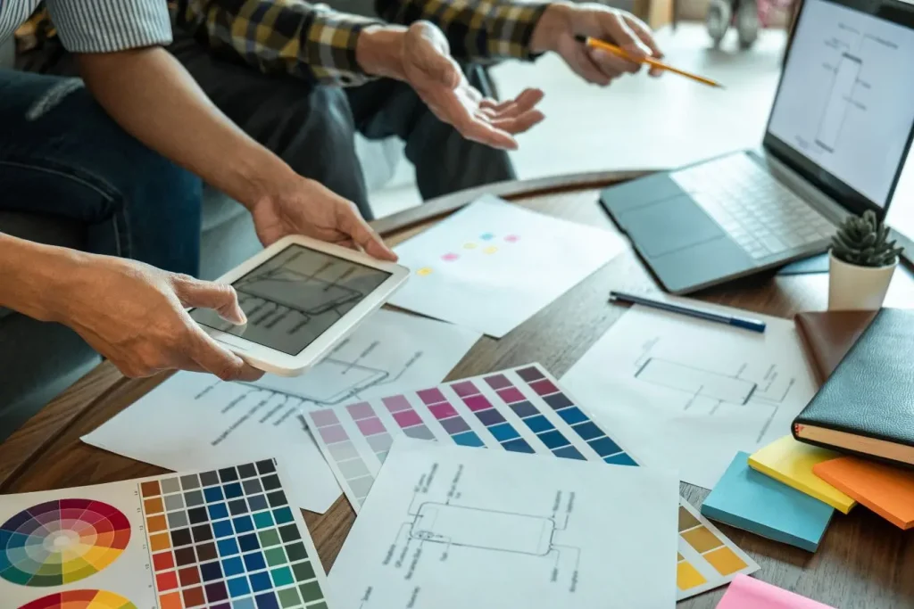 Deux personnes collaborent sur table avec palettes de couleurs et schémas, image qui illustre la pratique du UX writing dans la conception.