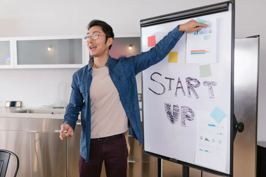Personne en chemise bleue présentant tableau blanc avec mot START UP, reflet du comparatif Incubateur vs Accélérateur de startup.