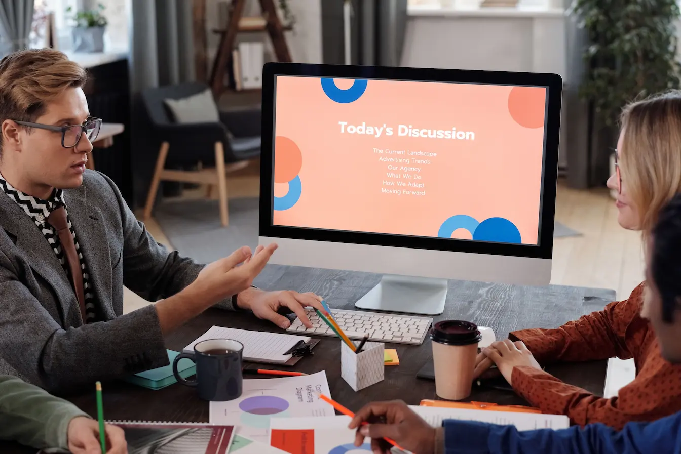 Groupe en réunion autour de table avec graphiques et café, reflet d’une présentation structurée typique d’un pitch deck.