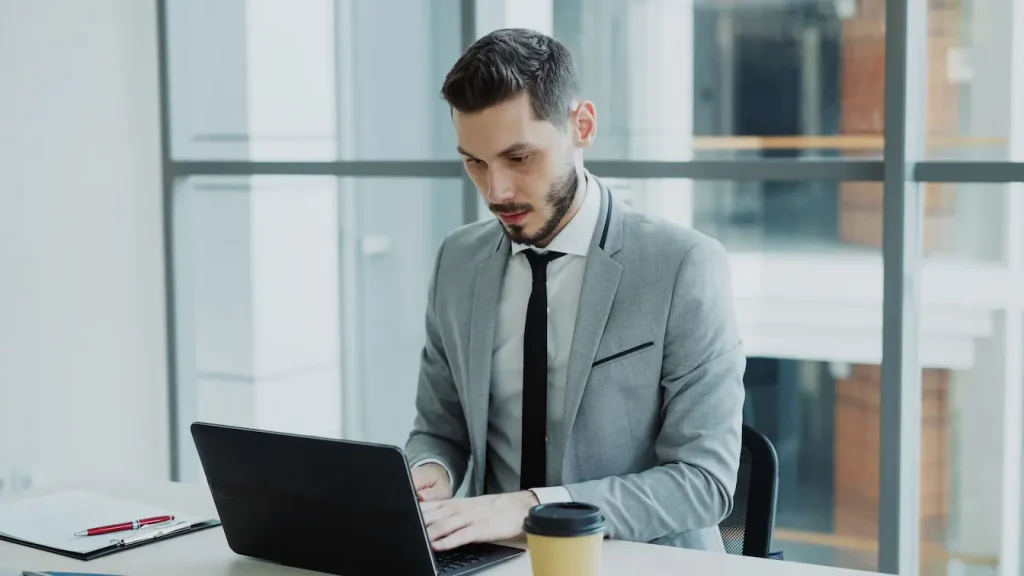 Personne en costume gris travaillant sur laptop dans bureau moderne, reflet des enjeux liés au statut auto-entrepreneur en 2026.