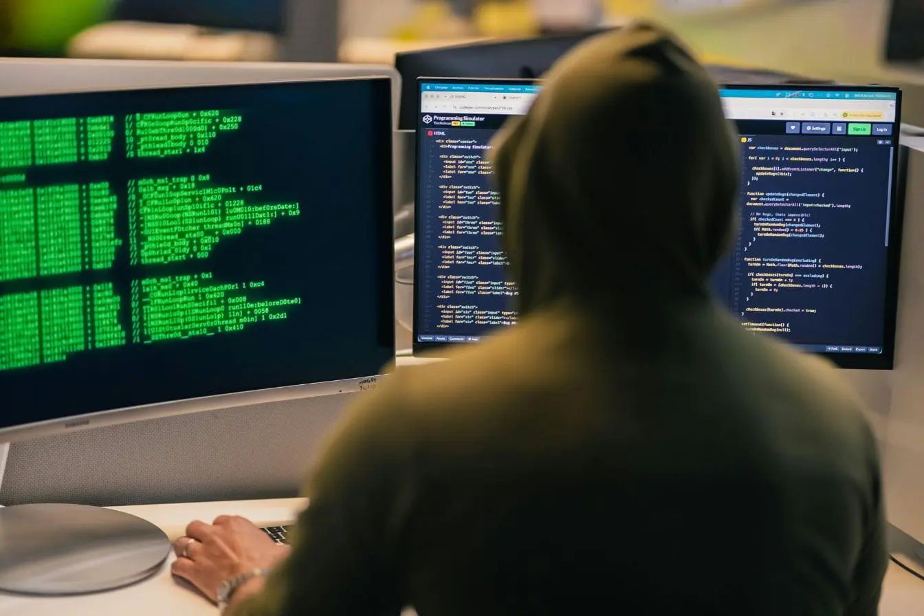 growth hacking Personne en hoodie devant deux écrans affichant code vert et éditeur, reflet des stratégies de growth hacking basées sur analyse et optimisation digitale.