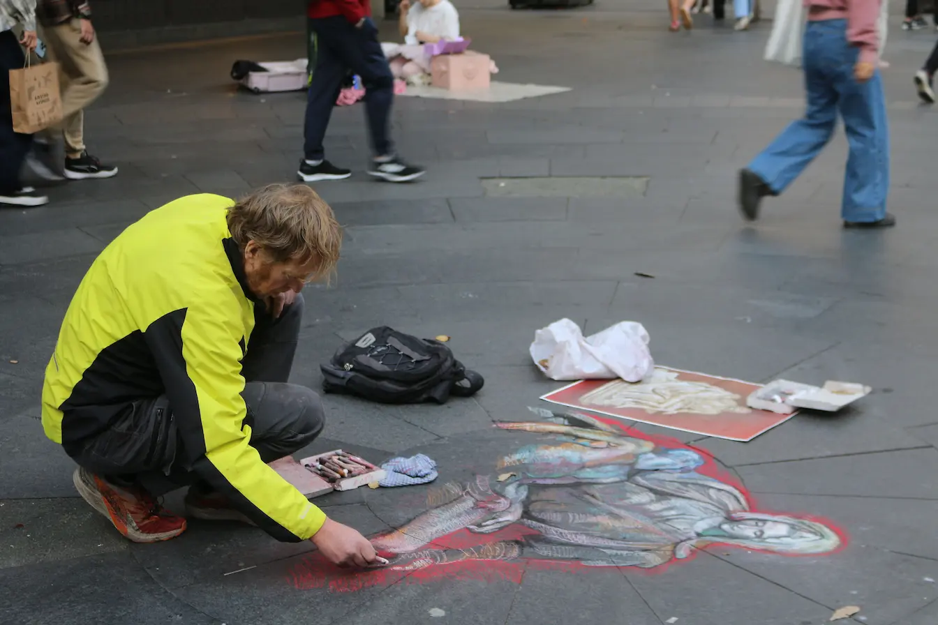 guérilla marketing créative Artiste en veste jaune dessinant à la craie sur trottoir, image qui illustre une action de guérilla marketing créative et urbaine.