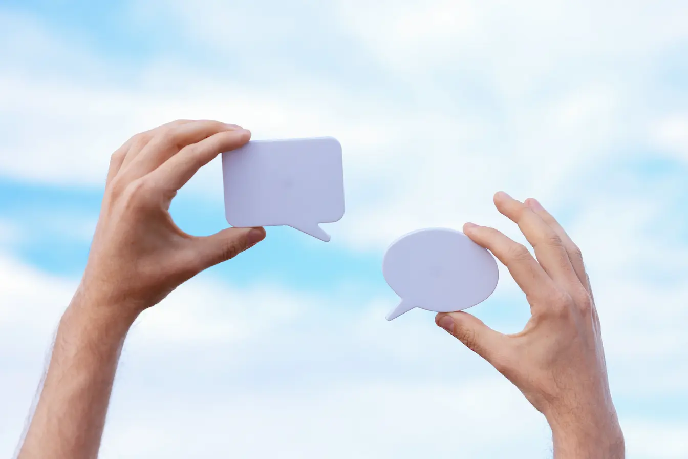 marketing conversationnel Deux mains tenant des bulles de dialogue blanches sur fond bleu, image qui illustre le marketing conversationnel et l’usage des chatbots.