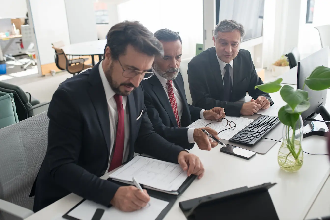 pacte d’actionnaires Trois personnes en réunion professionnelle discutent de documents, image qui illustre le pacte d’actionnaires et ses clauses essentielles à intégrer absolument.