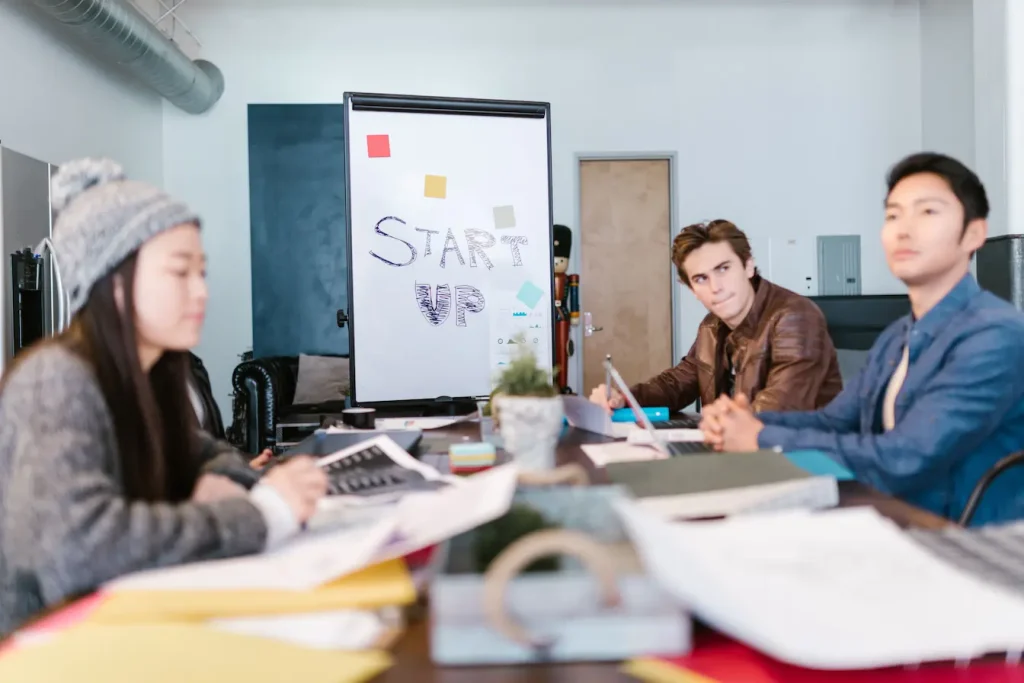 Trois personnes en réunion autour de table avec laptops et dossiers, reflet d’un pitch deck en préparation pour une startup.