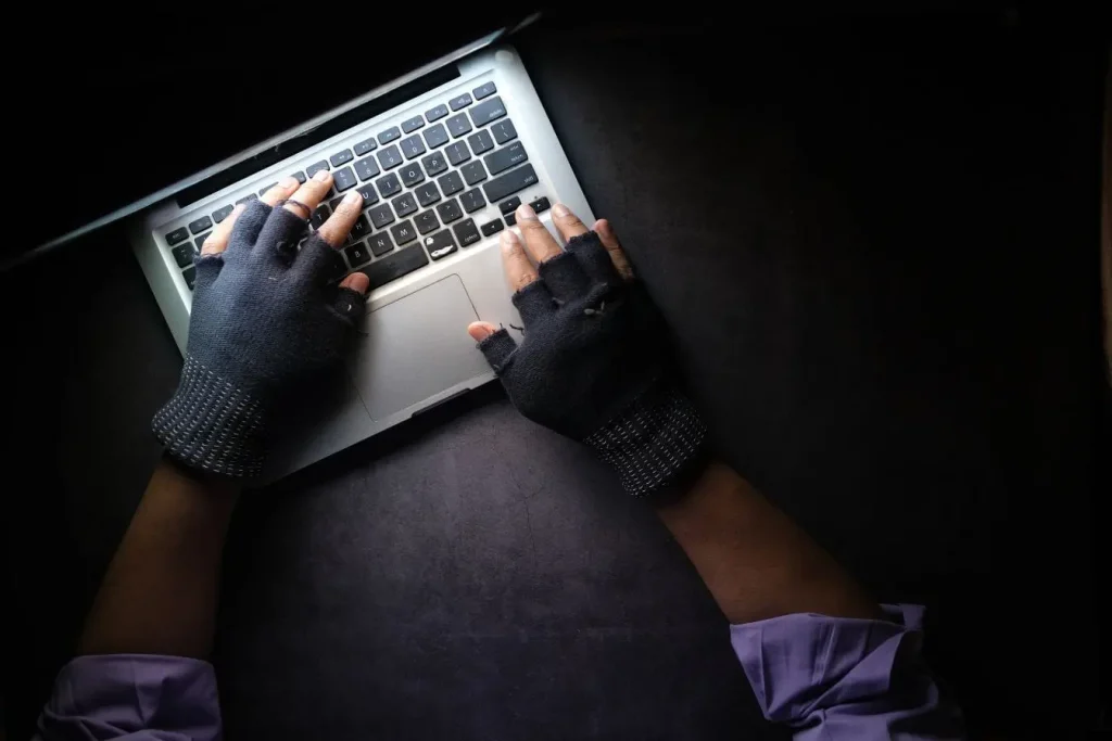 Mains gantées tapant sur clavier d’ordinateur portable dans lumière sombre, reflet des pratiques de growth hacking basées sur tests rapides et optimisation digitale.