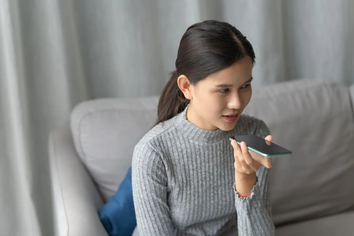 voice search Gros plan sur main tenant téléphone près de la bouche, image claire illustrant l’interaction voice search et SEO.