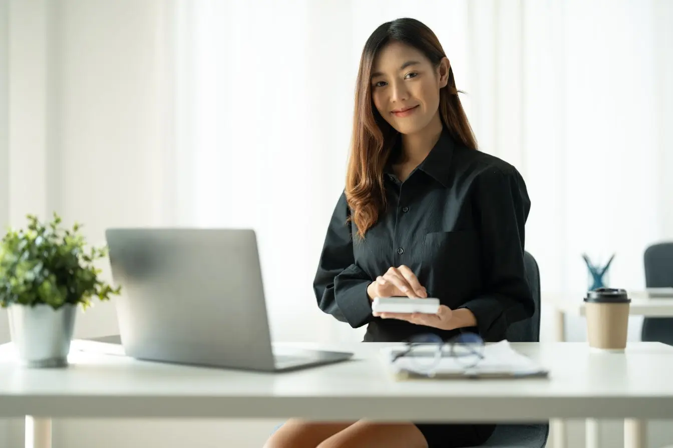 Account Based Marketing Une professionnelle souriante assise devant son ordinateur portable dans un bureau lumineux, illustrant une stratégie de Account Based Marketing.