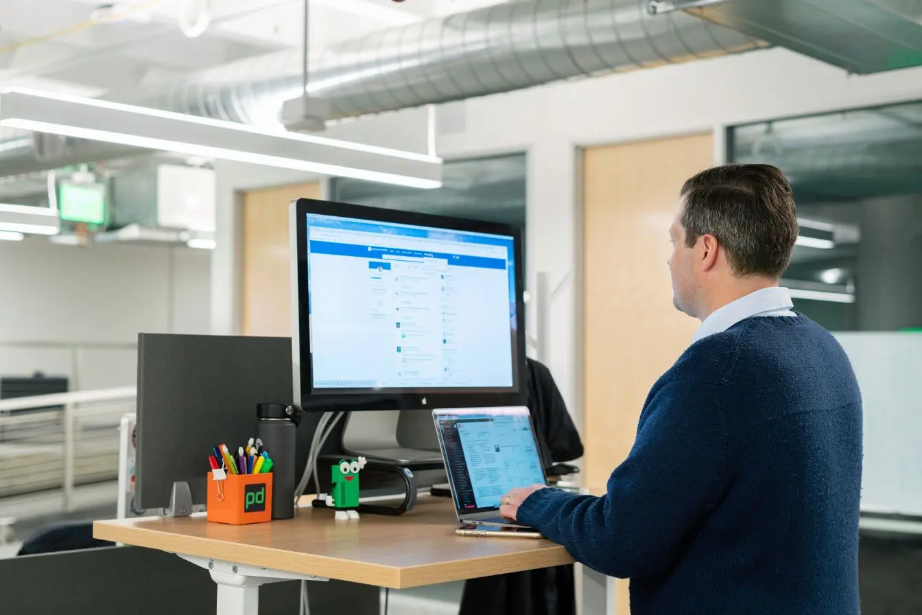 LinkedIn Un professionnel travaillant debout devant son bureau à un ordinateur pour mener sa stratégie de prospection LinkedIn dans un espace lumineux.