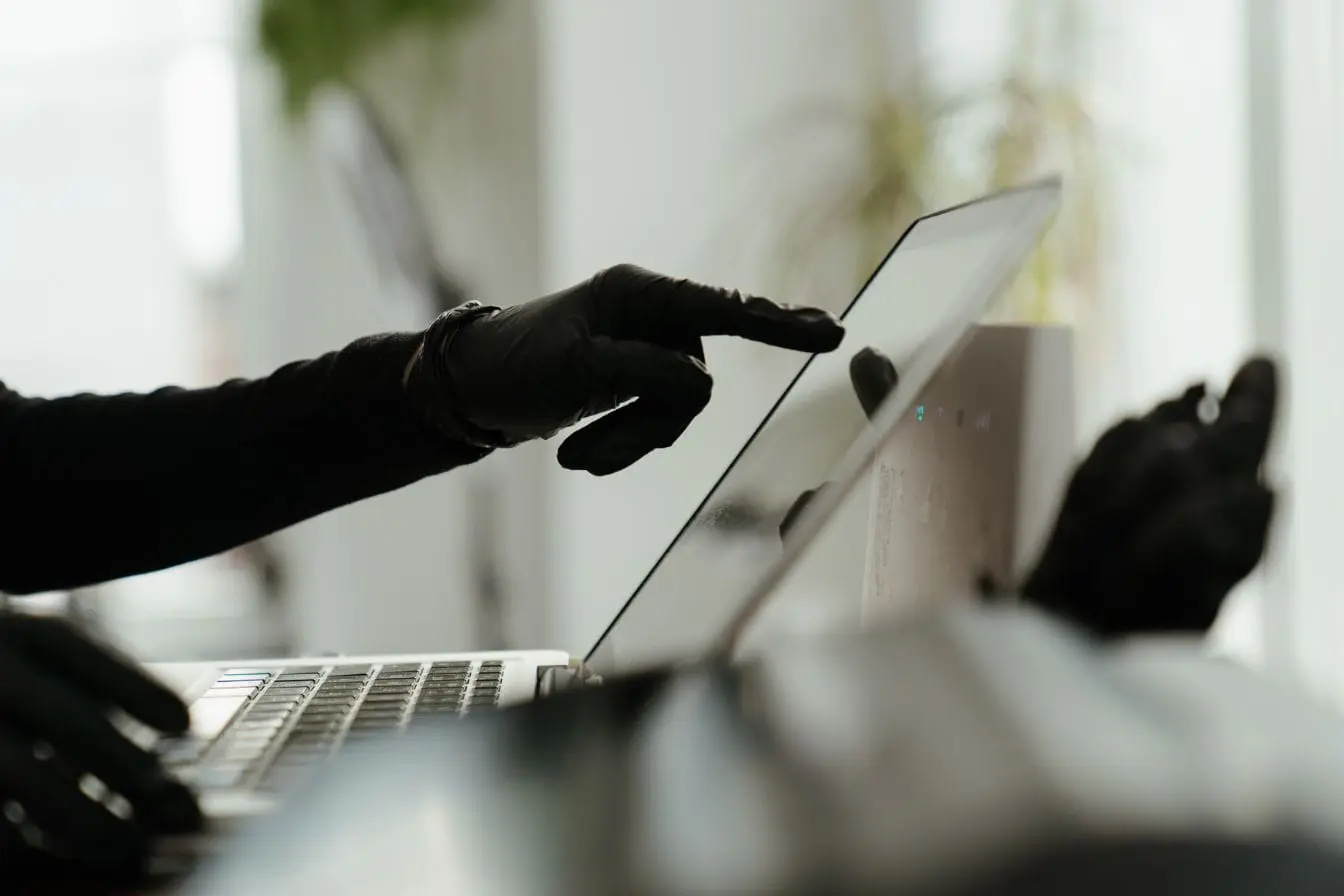 Gros plan sur mains gantées utilisant écran tactile et clavier, symbole des précautions contre le phishing et l’hameçonnage en ligne.