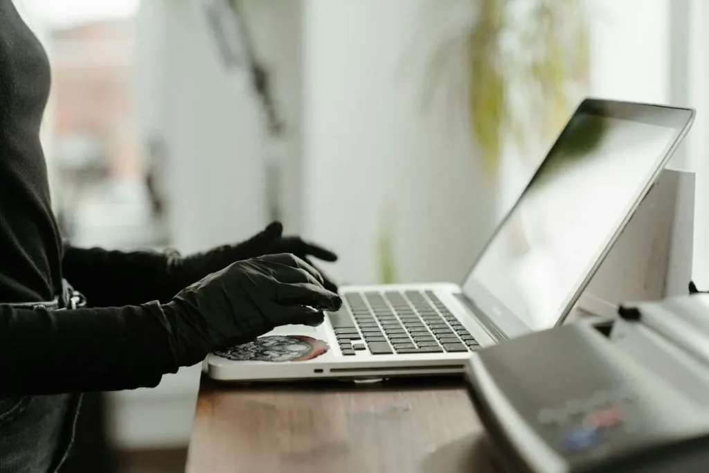 Personne en gants noirs tapant sur ordinateur portable argenté, symbole des précautions contre le phishing et l’hameçonnage en ligne.
