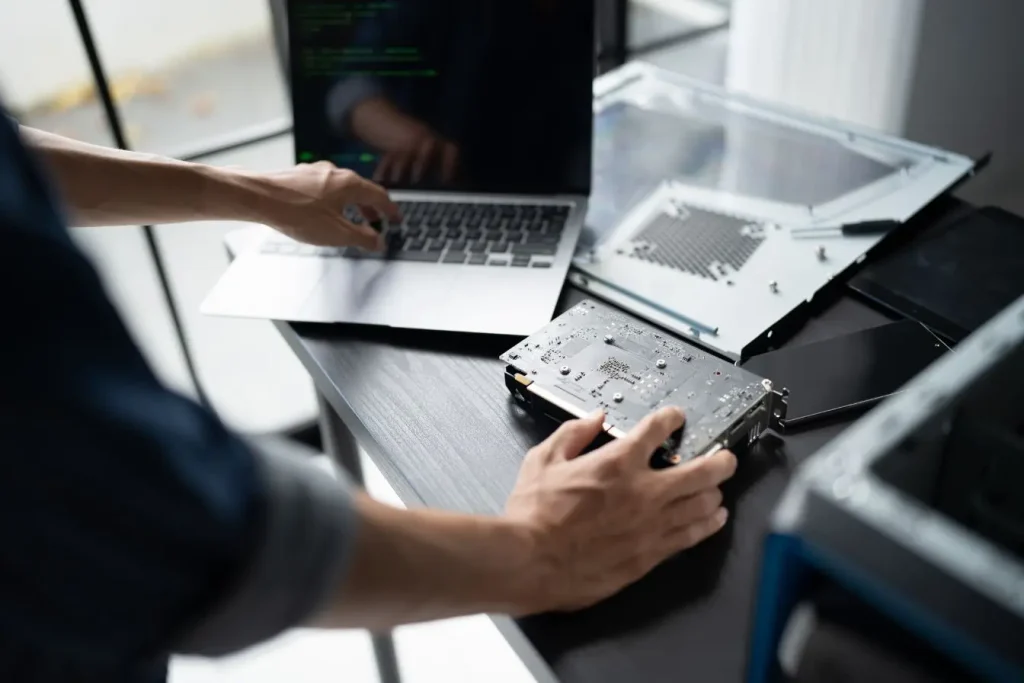 Technicien manipulant du matériel informatique et des composants ouverts sur un bureau, illustrant la dette technique qui complique la maintenance des projets