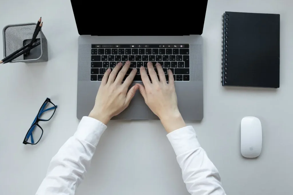 Une personne tapant sur le clavier d'un ordinateur portable gris sur un bureau bien rangé pour illustrer le copywriting et techniques de persuasion.