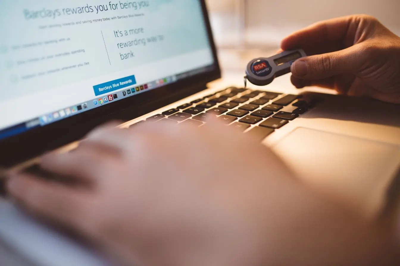 sécurité en ligne Gros plan sur main tenant jeton RSA devant clavier d’ordinateur, symbole de l’authentification à deux facteurs pour sécuriser l’accès bancaire en ligne.